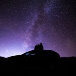 silhouette of person sitting on car under starry night