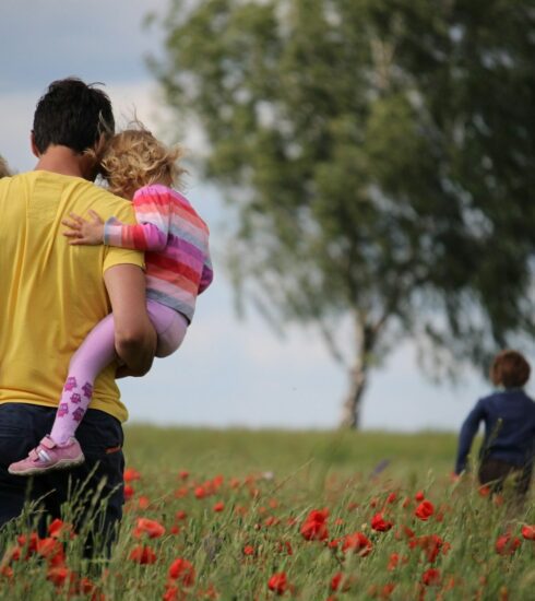 man carrying to girls on field of red petaled flower