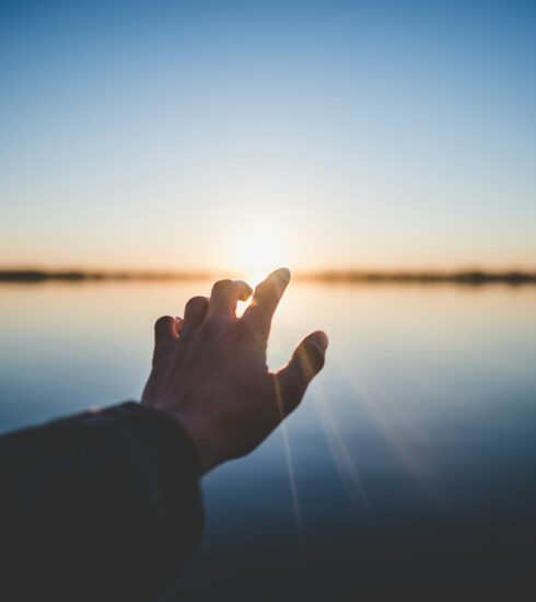 landscape photography of person's hand in front of sun